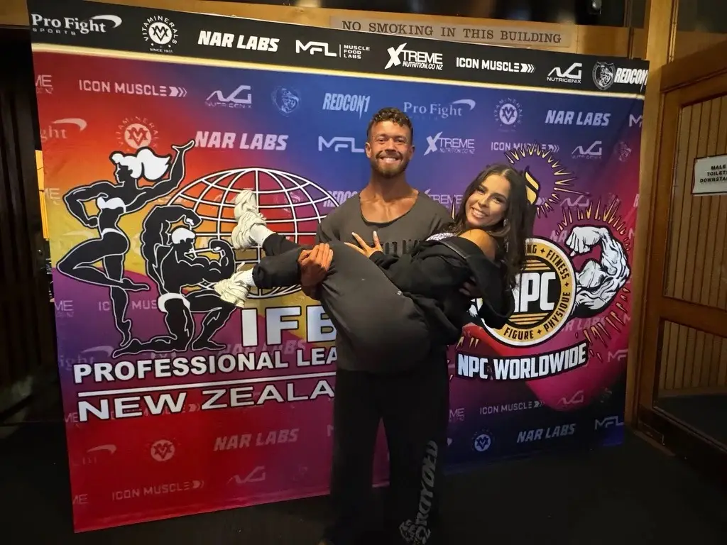 James and Abigail in front of the IFBB Pro League New Zealand banner